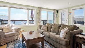 A living room with a sofa, armchairs, a coffee table, and a view of the sea through large windows. - Oceanfront Getaway with Deck, Steps to Provincetown Fun (Provincetown)