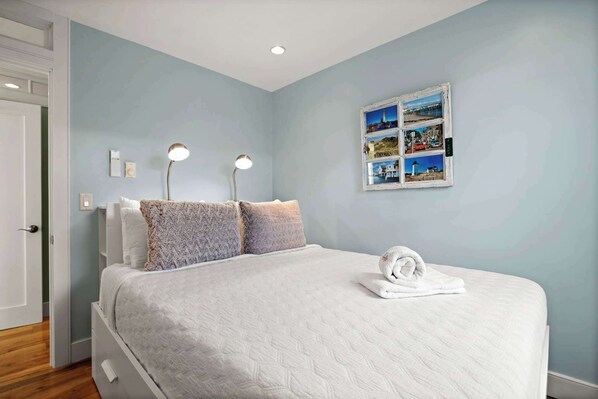 A neatly made bed with a white duvet and fluffy pillows, two bedside lamps, and a wall-mounted photo collage. - Oceanfront Getaway with Deck, Steps to Provincetown Fun (Provincetown)