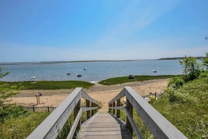 A wooden staircase leading to a beach with boats in the water and a clear sky.