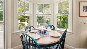 Un comedor con una mesa redonda, cuatro sillas y un ventanal con contraventanas blancas.