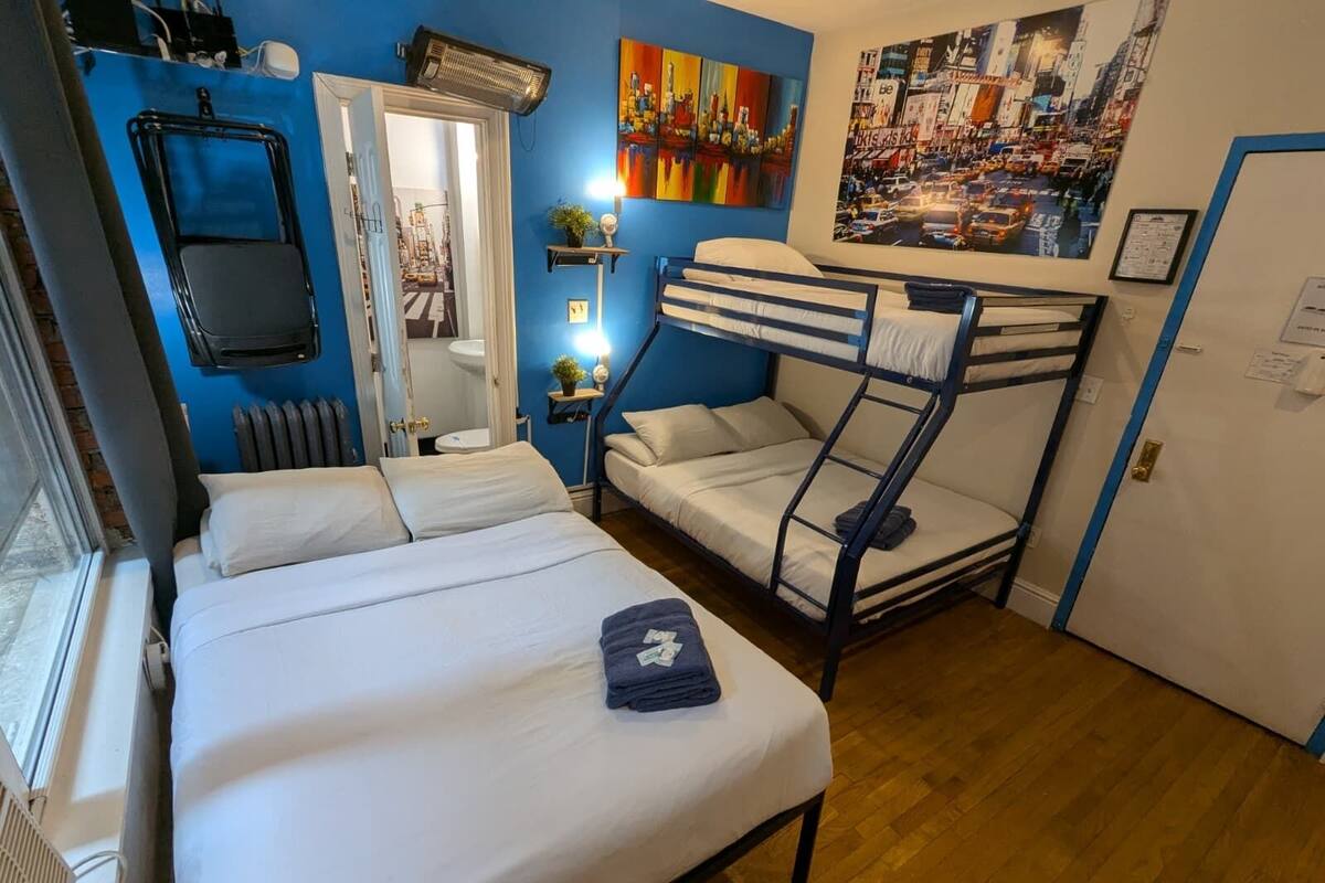 A compact room with a bunk bed, a single bed, a radiator, a mirror, and a door leading to a bathroom.