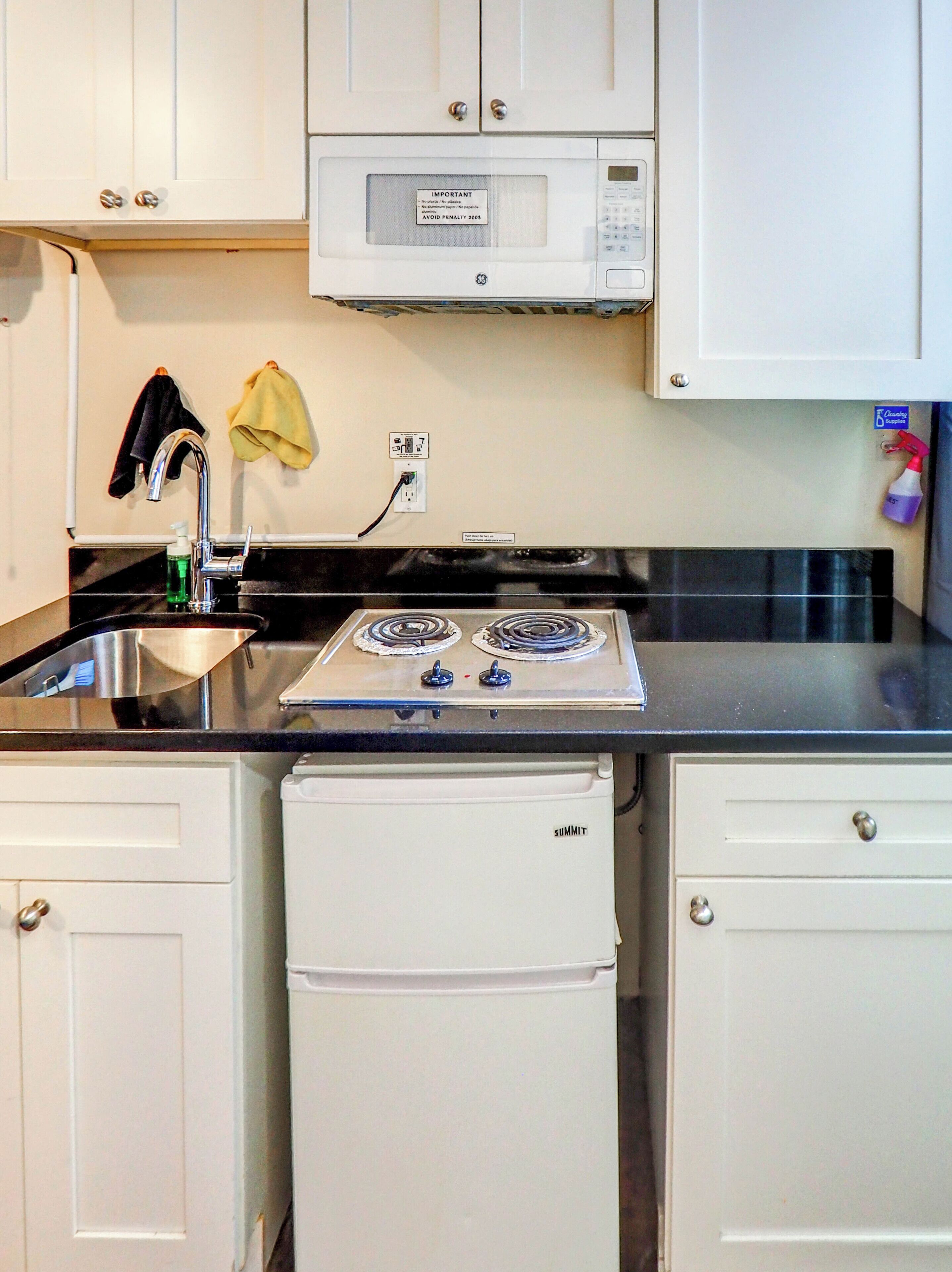 A kitchen with white cabinets, a stainless steel sink, a microwave, a stove, and a refrigerator.