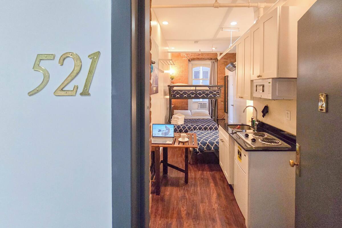 A compact room with bunk beds, a kitchenette, and a small desk with a laptop.