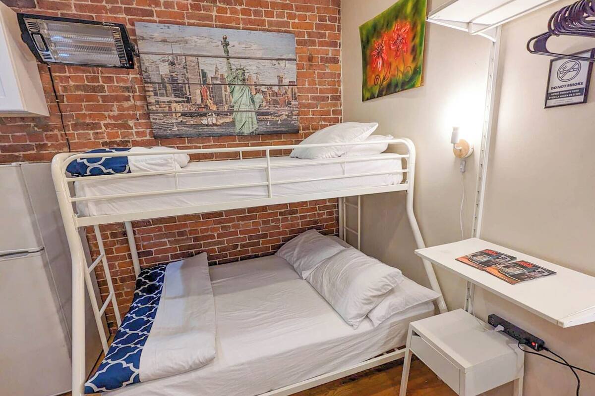 A bunk bed with a desk and chair, a heater, and a painting of the Statue of Liberty.