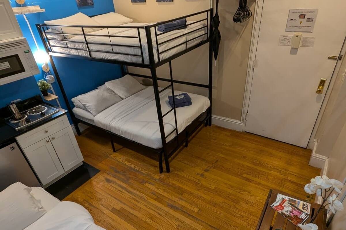 A bunk bed room with a kitchenette, a small table with an orchid, and a door with a sign.
