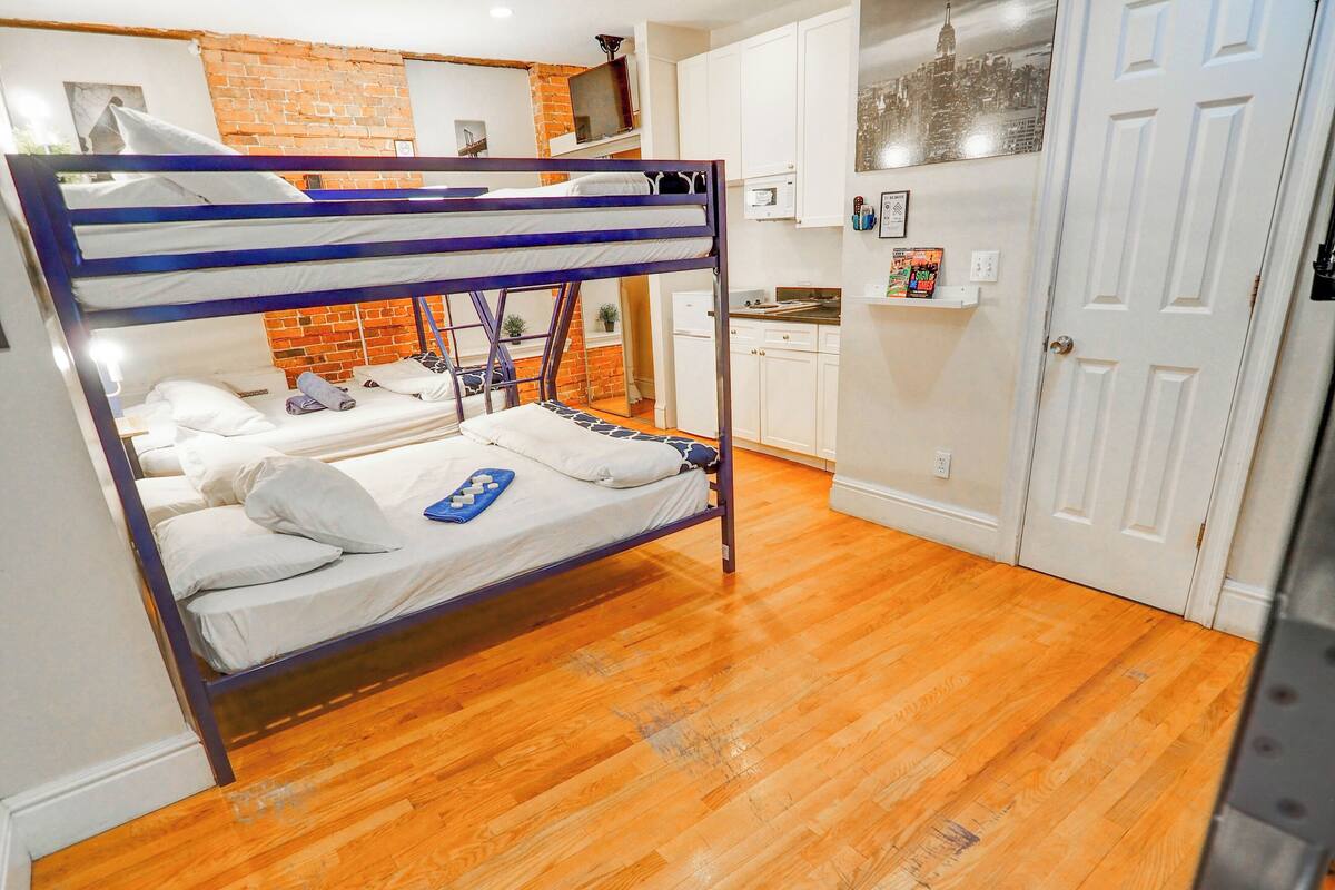 A bunk bed with white bedding and a blue towel, a kitchen area with white cabinets, and a door with a cityscape picture.