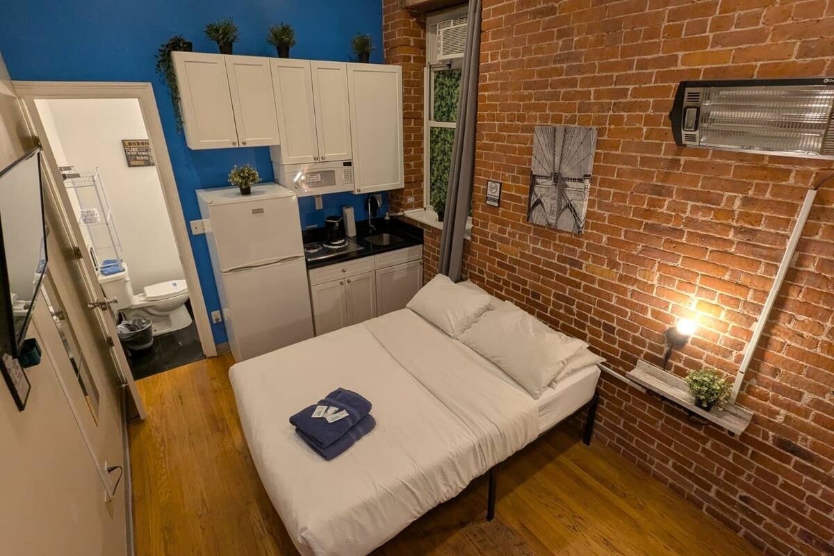 A compact room with a bed, a kitchenette, and a bathroom.