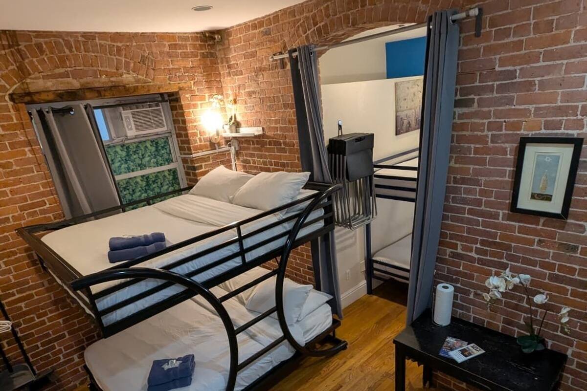 A compact room with a bunk bed, a small table with a vase, and a brick wall.