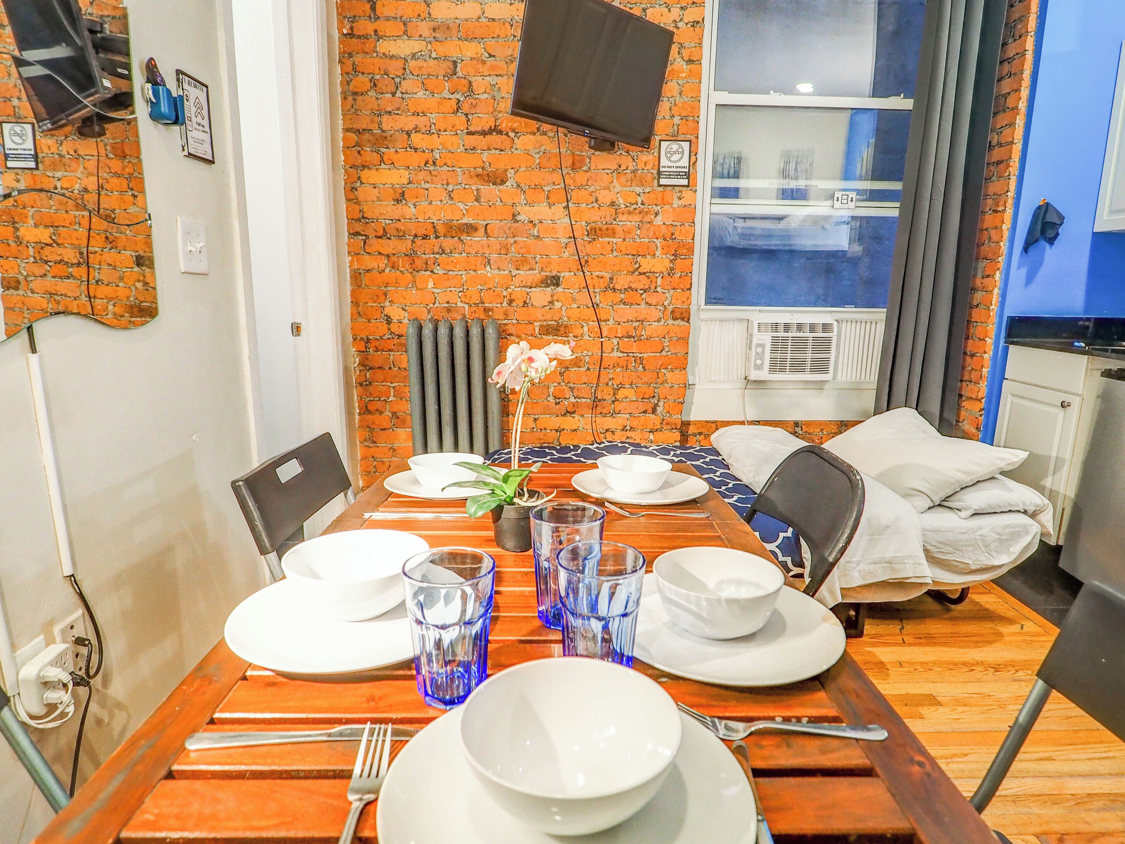 A dining area with a brick wall, a table set with plates, glasses, and a potted orchid.