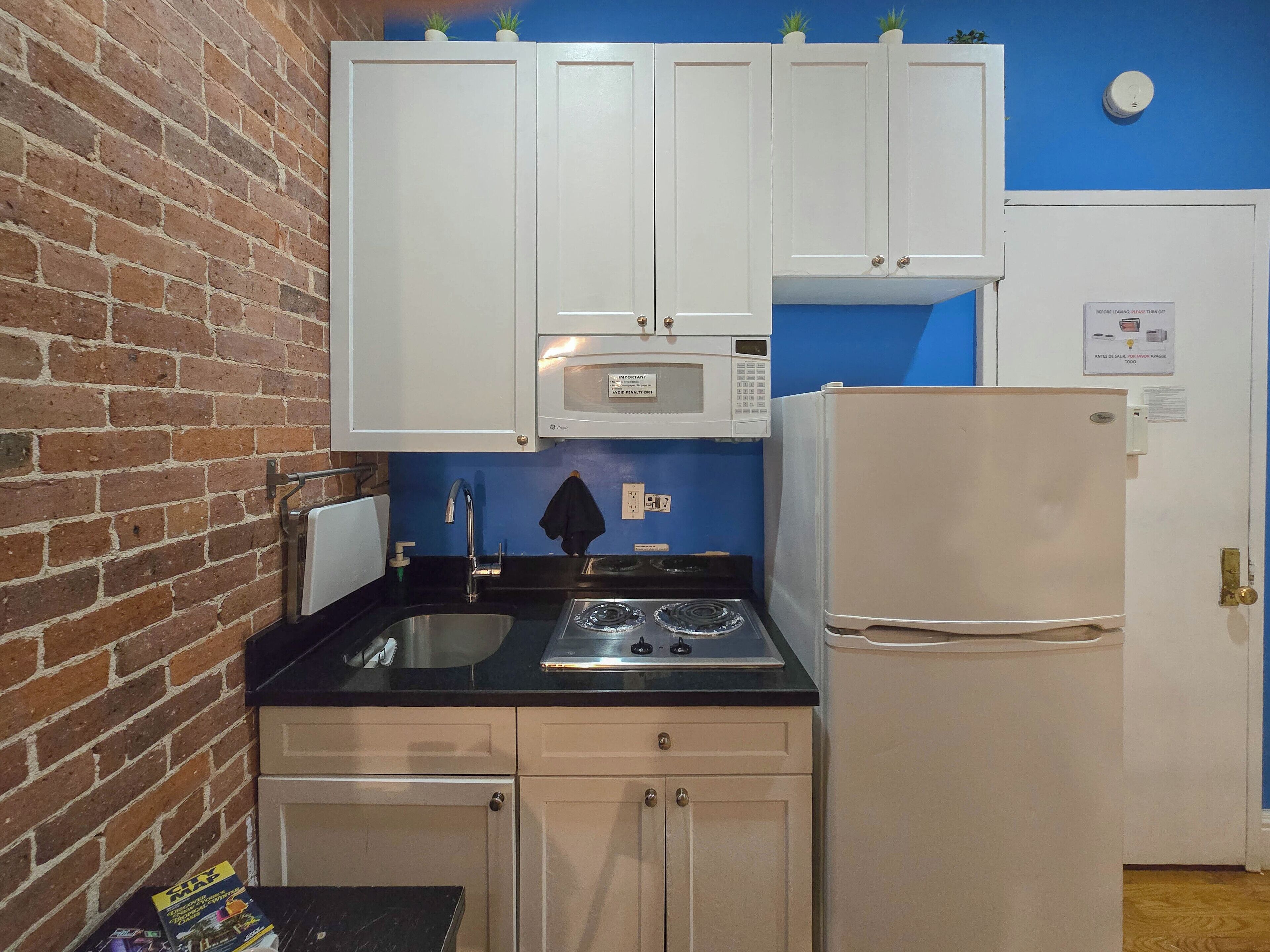 A compact kitchen with white cabinets, a black countertop, a stainless steel sink, a microwave, a stove, and a refrigerator.