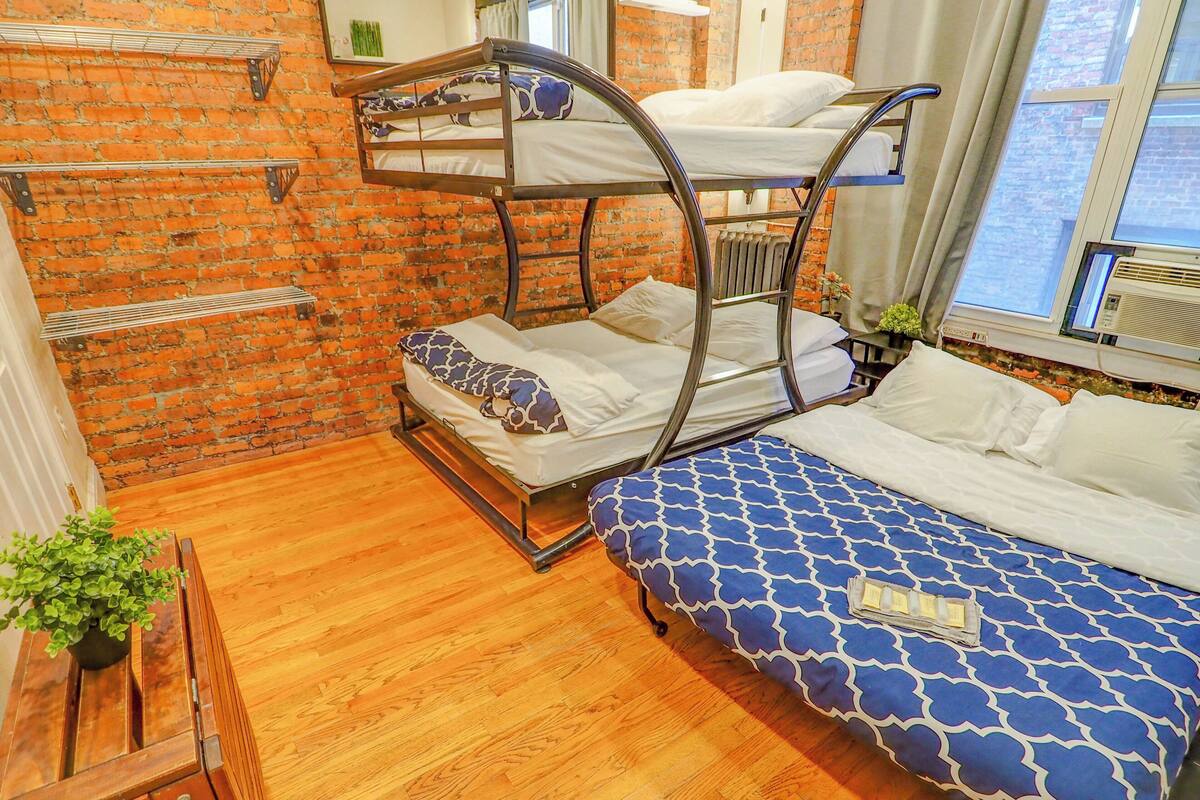 A bunk bed room with a brick wall, wooden floor, and a window with curtains.