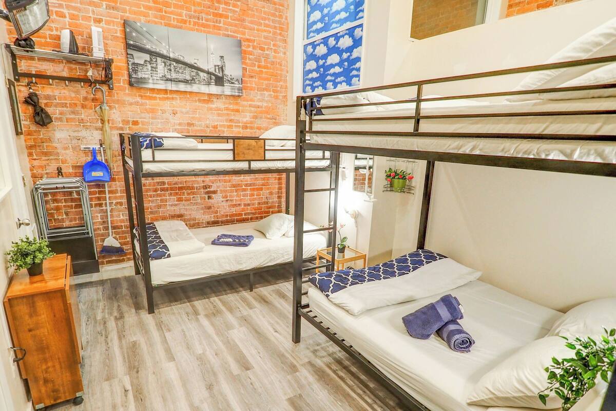 A dormitory room with bunk beds, a brick wall, a cityscape painting, and a window with a cloud pattern.