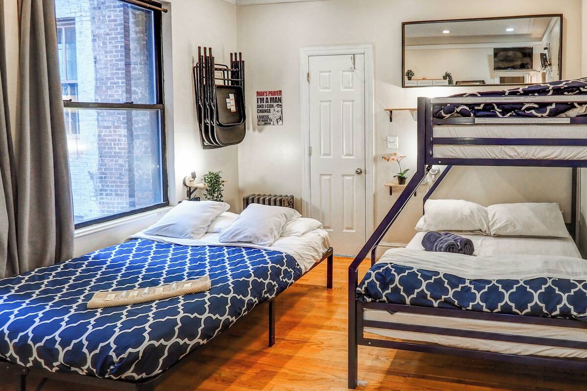 A room with two bunk beds, a window with curtains, a radiator, a door, and a mirror on the wall.