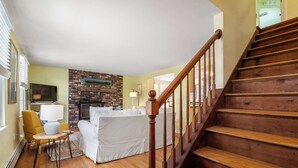 A living room with a fireplace, a sofa, a chair, and a wooden staircase. - Walk to Water, near Downtown Chatham! (Chatham)