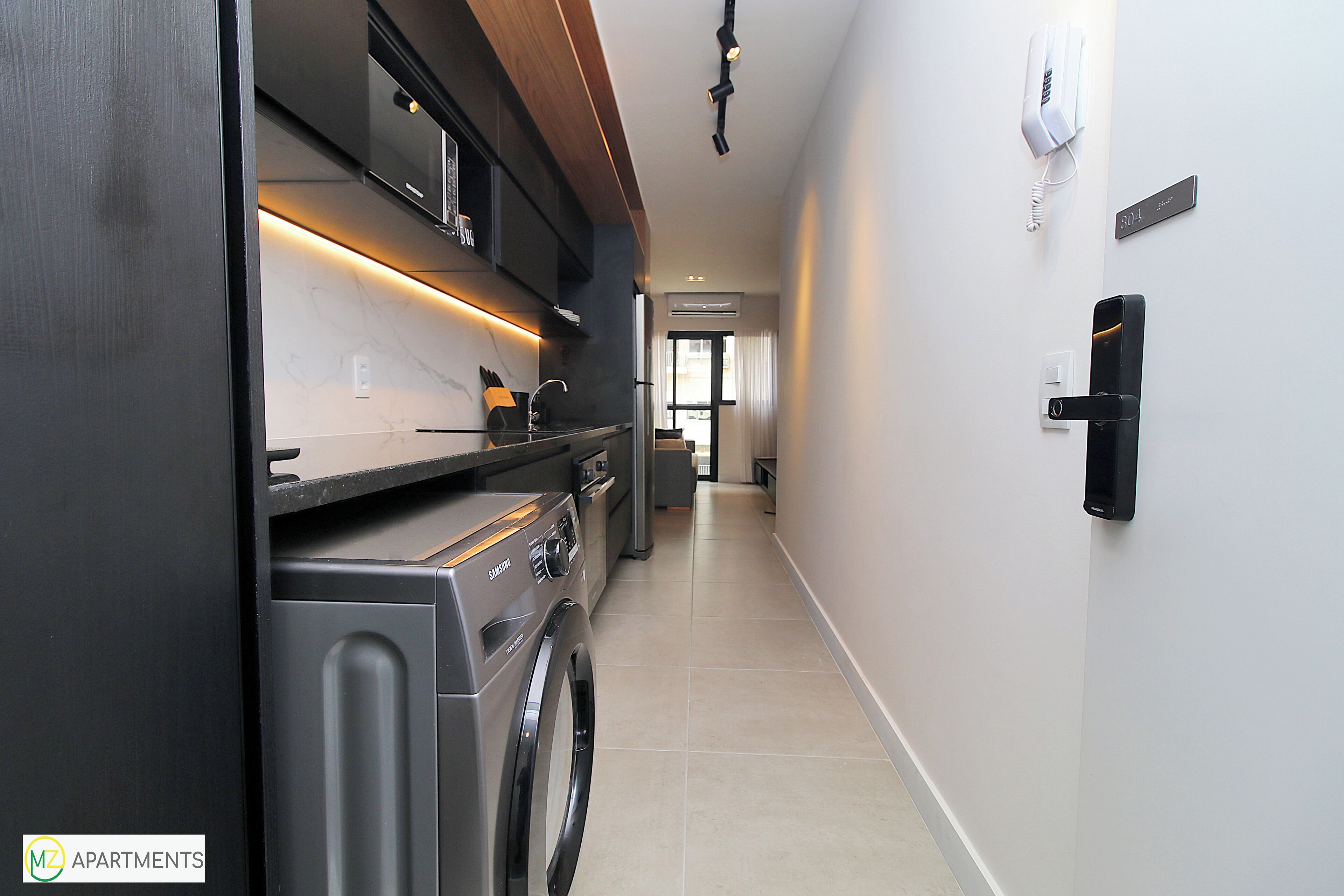 A modern kitchen with a built-in washer and dryer, a wooden countertop, and a bright, well-lit hallway.