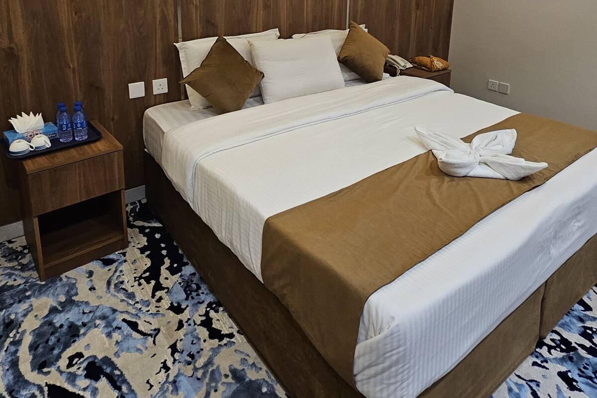 Hotellihuone, jossa on suuri sänky, puinen pääty, yöpöydät ja kuviollinen matto.