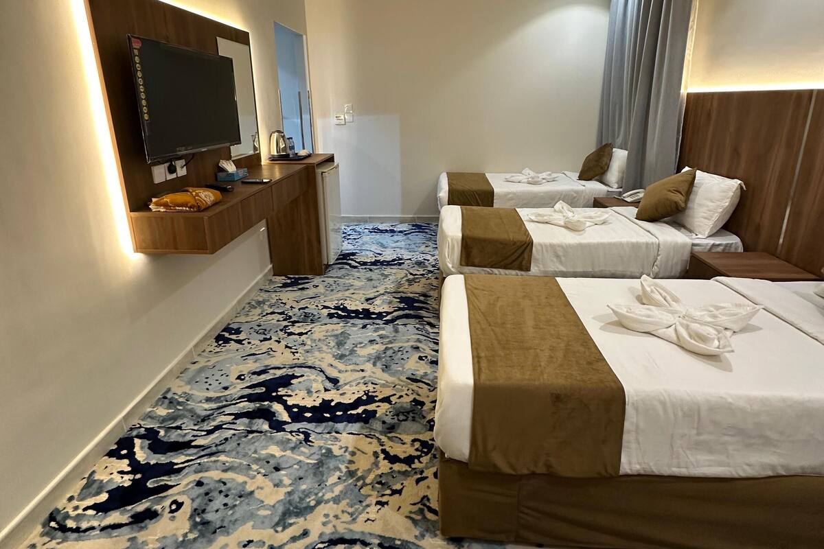 Hotellihuone, jossa on suuri sänky, pienempi sänky, työpöytä, jossa on televisio, ja kuviollinen matto.