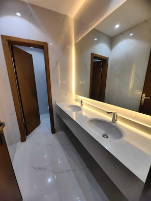 A modern bathroom with two sinks, a large mirror, and a wooden door. - Abeer Al Azizia Hotel (Makkah)