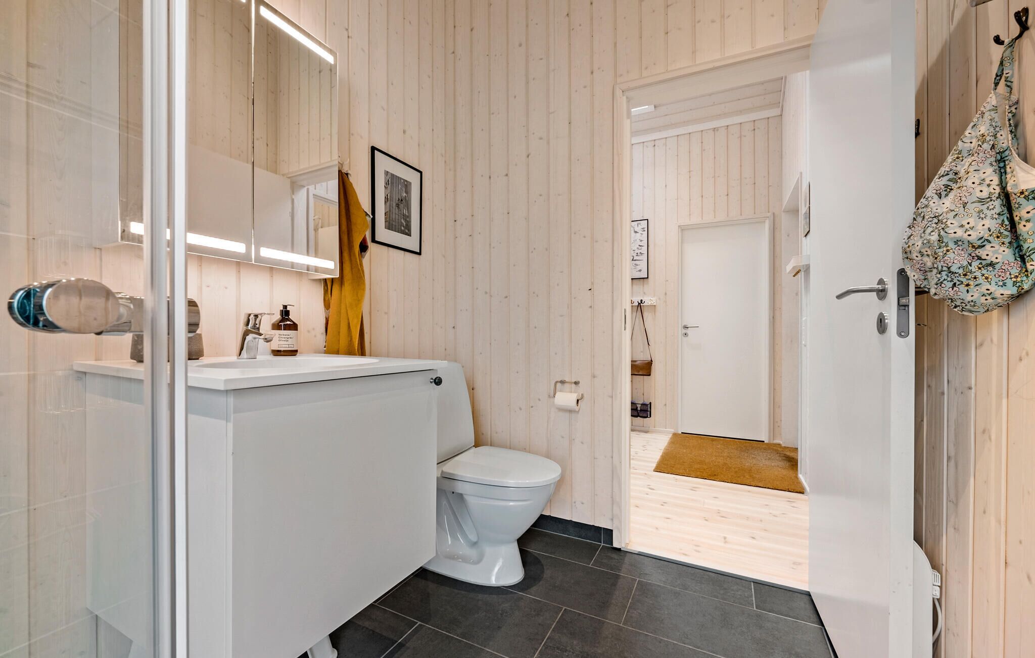 Ein modernes Badezimmer mit Toilette in Weiß, einer Duschkabine aus Glas und einer Holzwand.