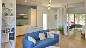 A modern living room with a blue sofa, a white coffee table, and a kitchen area with a fridge and sink. - Perla Modern Penthouse 217 (Gjiri Lalzit)