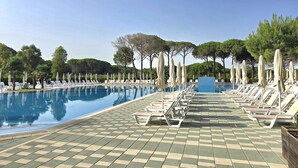 A pool area with lounge chairs and umbrellas, surrounded by trees and a clear sky. - Perla Modern Penthouse 217 (Gjiri Lalzit)