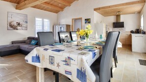 Uma área de refeições com uma mesa posta para quatro pessoas, um sofá e uma cozinha ao fundo.