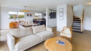 A spacious living area with a sofa, round coffee table, and dining table set for a meal. A staircase is visible in the background. - House for 10 - Garden - 600m from the beach (Penmarch)