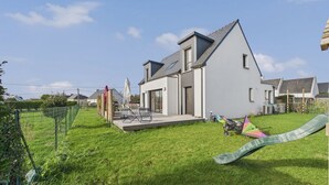 A modern house with a large backyard, a slide, and a patio area with outdoor furniture. - House for 10 - Garden - 600m from the beach (Penmarch)