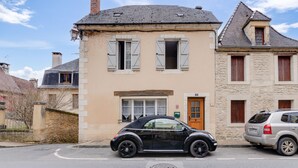Un immeuble de deux étages avec une façade beige et une voiture noire garée devant.