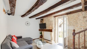 Un salon avec un canapé gris, une table basse en verre, une cheminée en pierre et un escalier en bois.