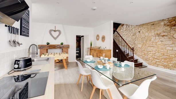 Une cuisine moderne avec une table à manger en verre, des chaises blanches et un mur en pierre.