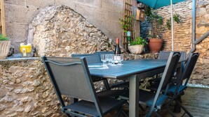 Une terrasse extérieure avec une table et des chaises, des murs en pierre et des plantes en pot.