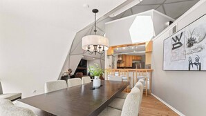 A modern dining area with a dark wooden table, light grey upholstered chairs, and a hanging light fixture. - Dome Manor / Pool + Hot Tub + Two Game Rooms (Bedford)