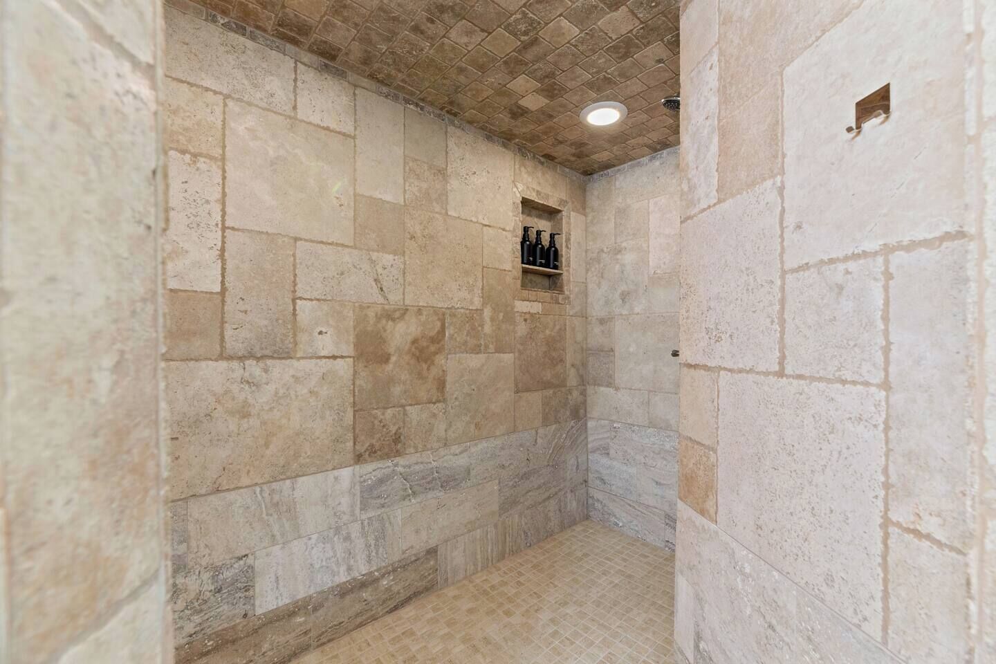 Ducha con paredes de piedra, piso de baldosas y luz empotrada en el techo.