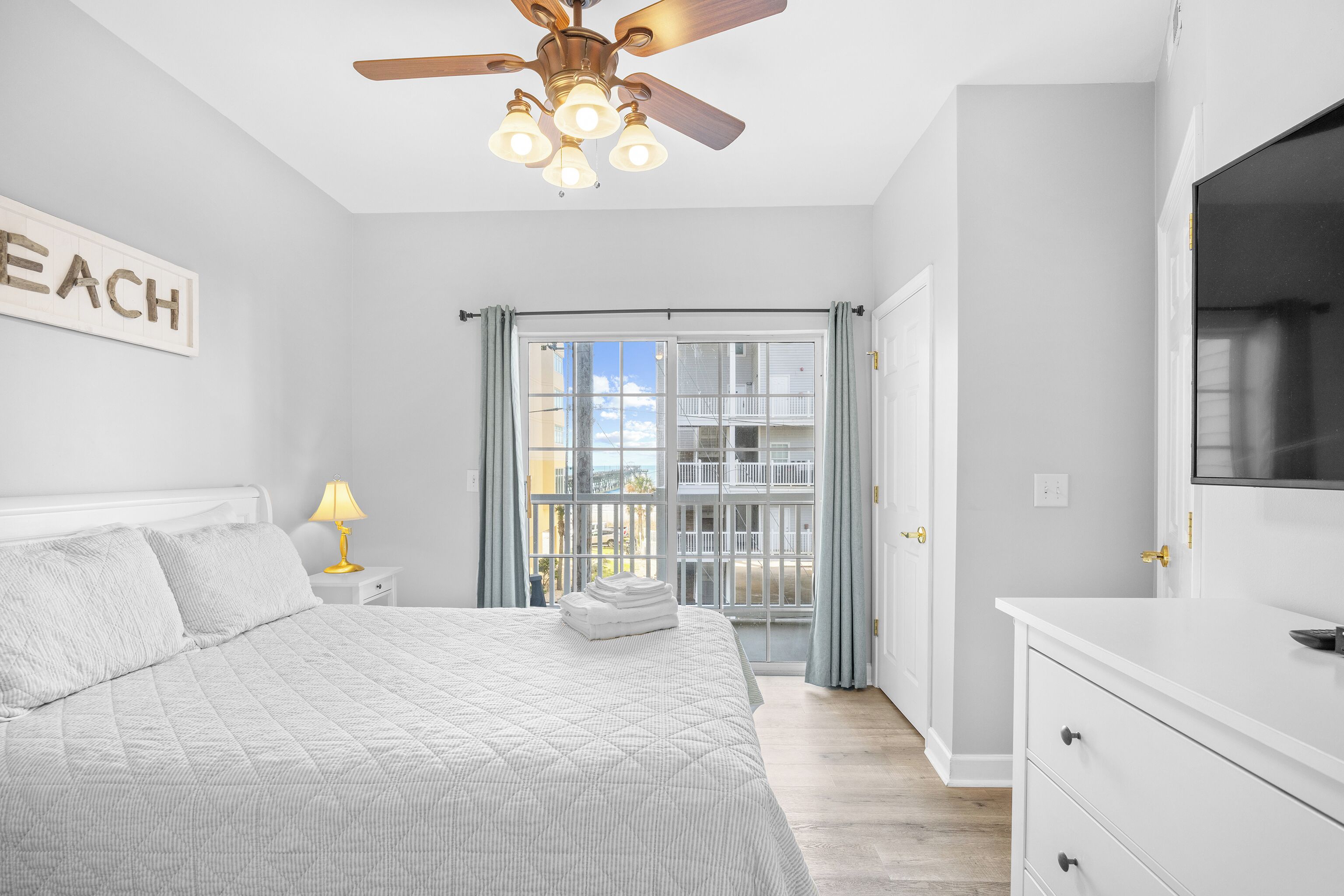 A bedroom with a bed, a ceiling fan, a nightstand with a lamp, and a window with curtains.