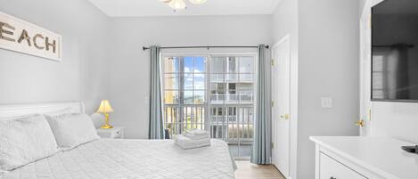 A bedroom with a bed, a ceiling fan, a nightstand with a lamp, and a window with curtains.