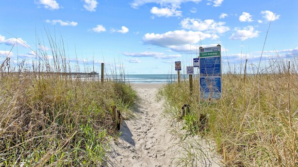 Ein sandiger Pfad führt zum Strand, ein Schild weist auf den Walkway 3310 hin.