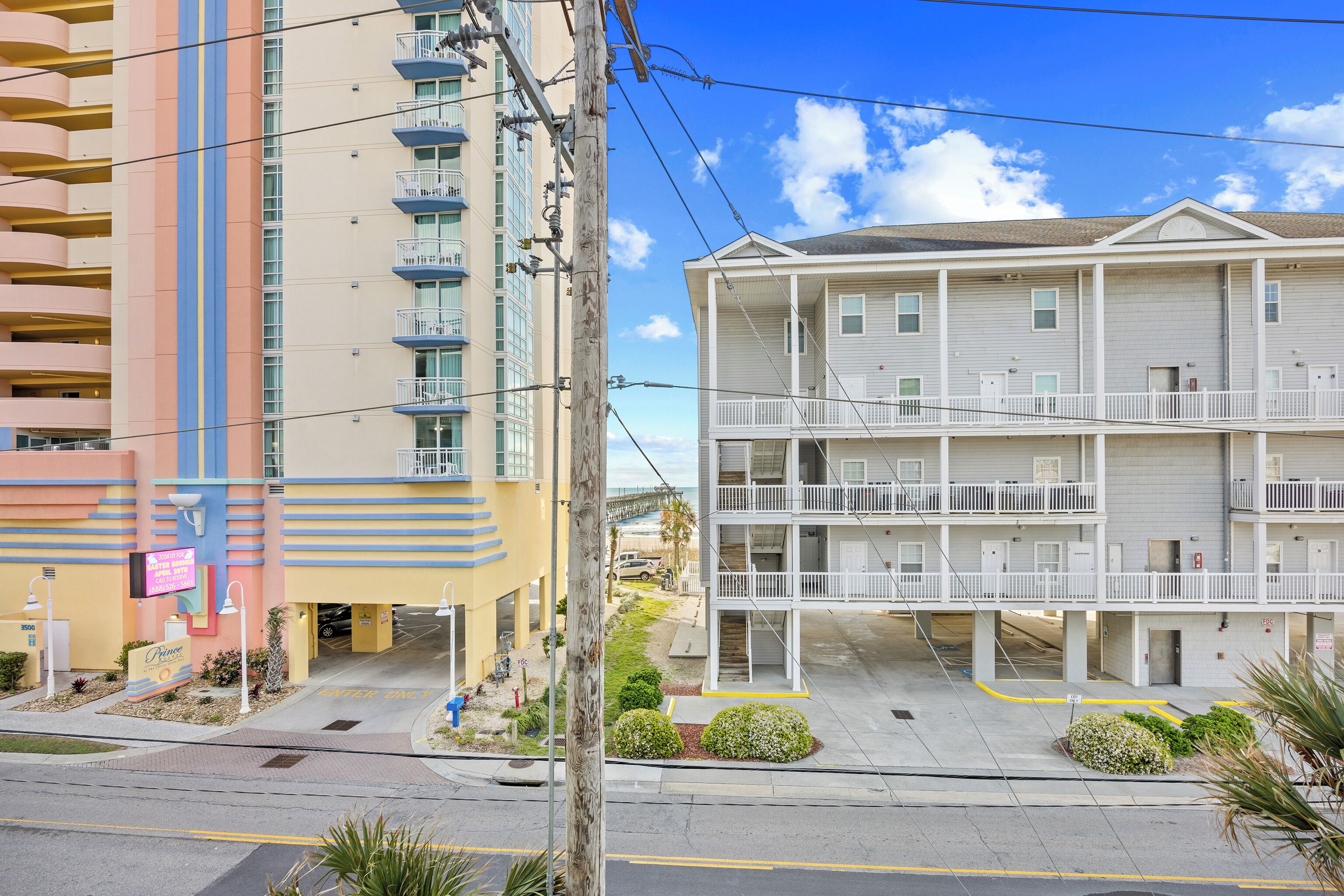 A multi-story hotel with balconies, a parking area, and a clear sky.
