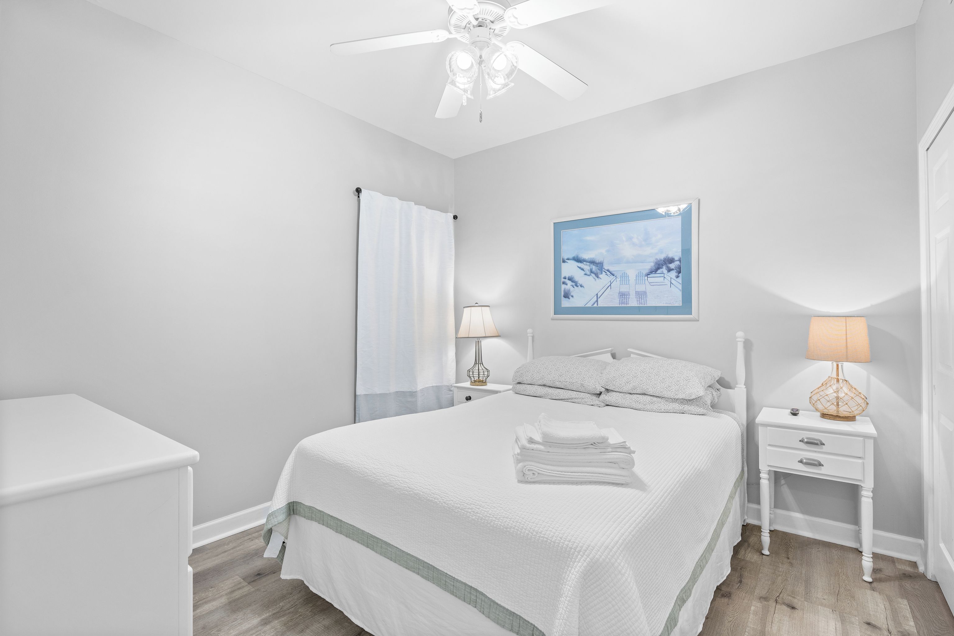 A bedroom with a bed, two bedside tables, a ceiling fan, and a wall-mounted lamp.