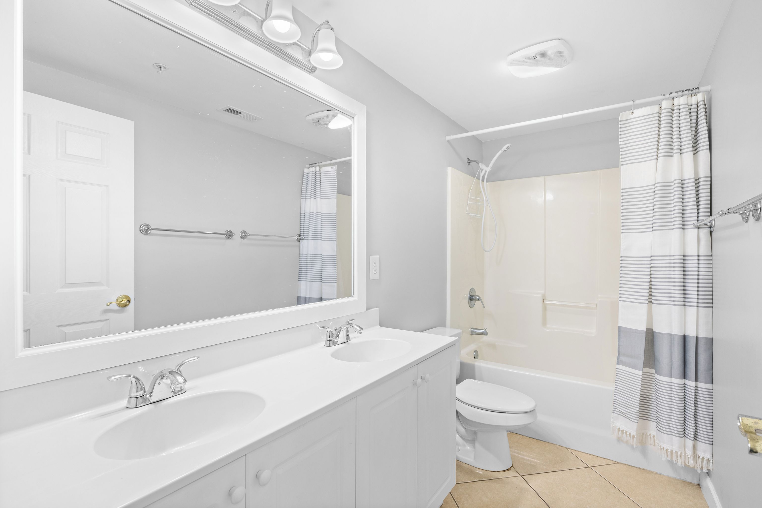 A modern bathroom with a large mirror, two sinks, a toilet, and a shower.