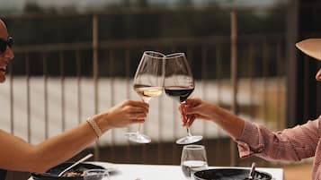 A dining table with a white tablecloth, two wine glasses, a hat, and a bowl of food.