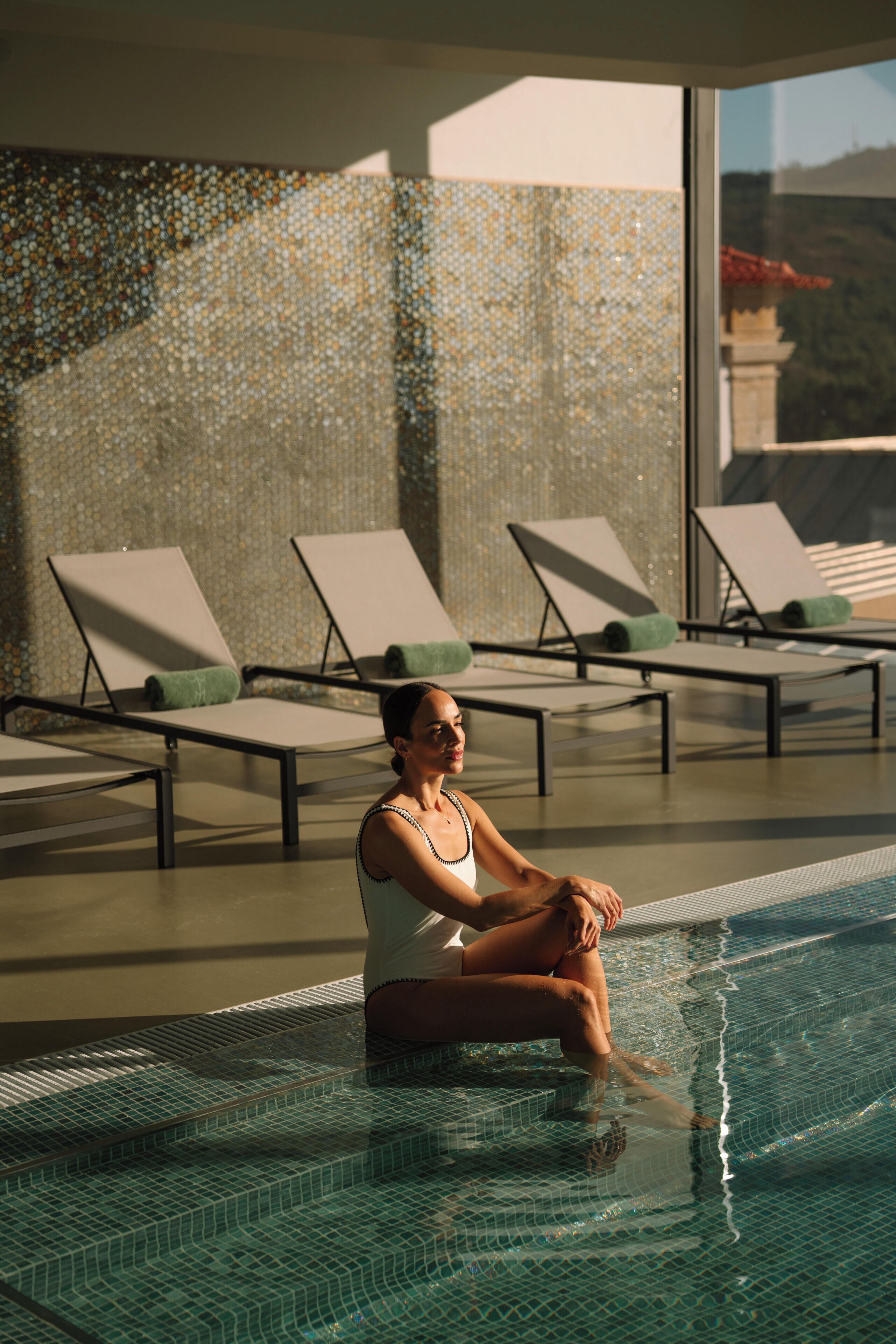 Un área junto a la piscina con sillones de descanso y una pared de azulejos.