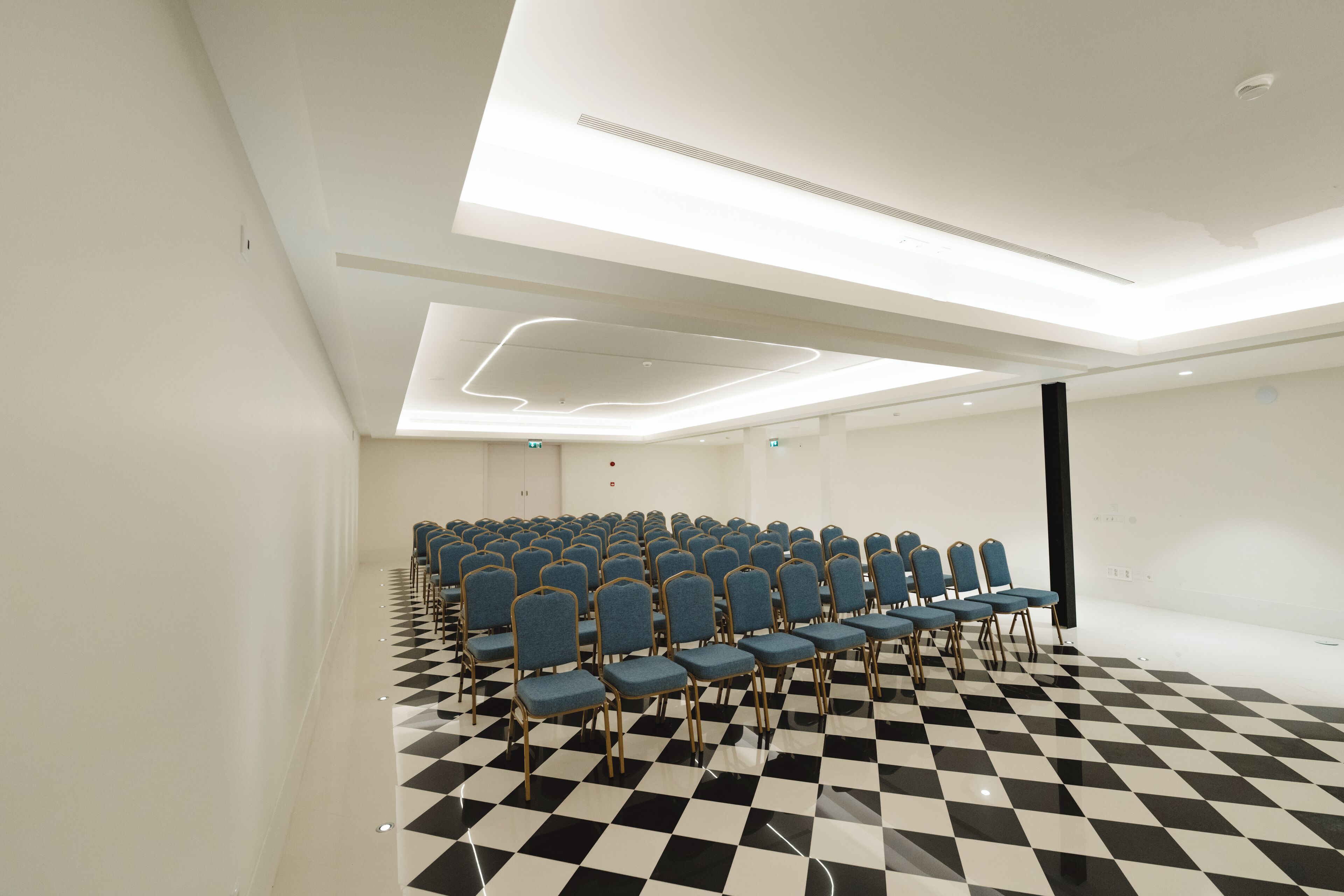 A conference room with rows of blue chairs, a black and white checkered floor, and a modern ceiling design.