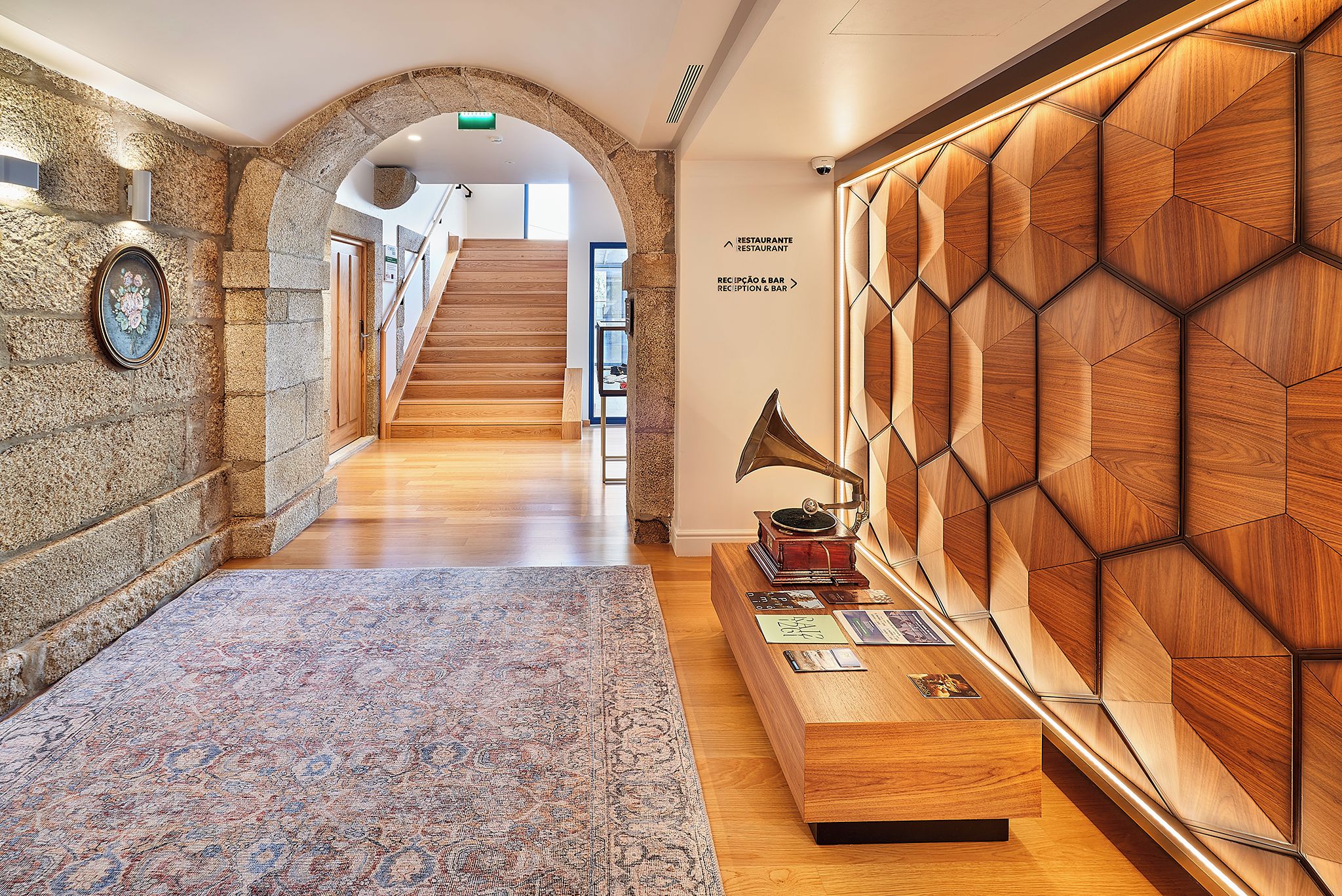 Eine Hotelhalle mit einer Rezeption, einem gemusterten Teppich, einer Treppe und einer Wand mit sechseckigen Holzpaneelen.