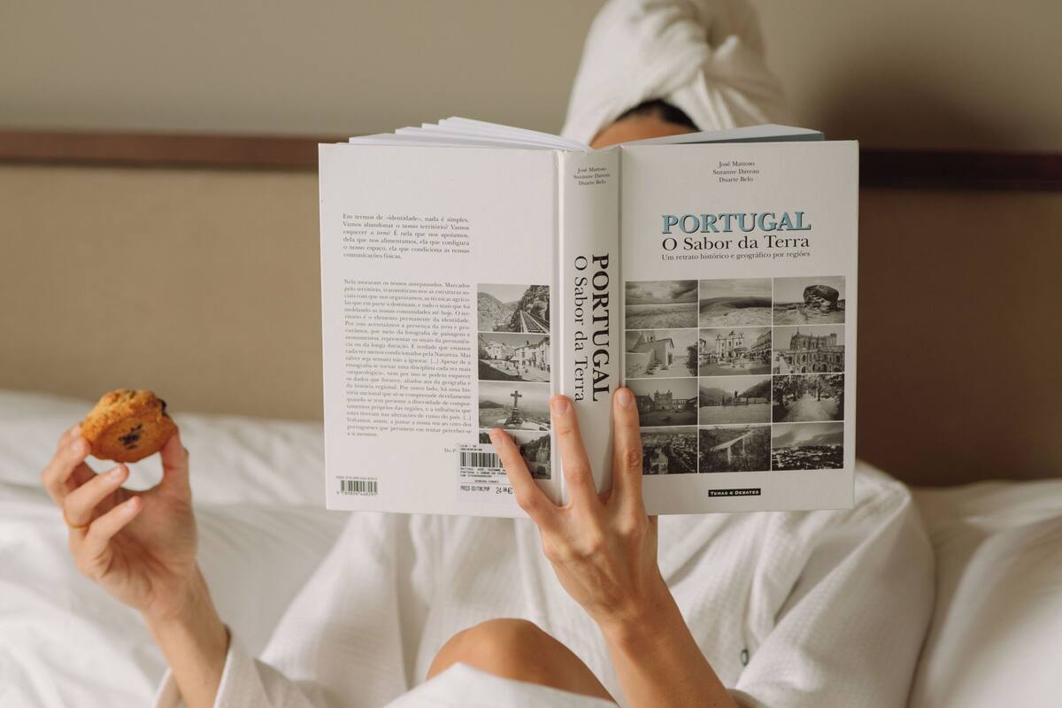 A person reading a book titled "Portugal O Sabor da Terra" in bed.
