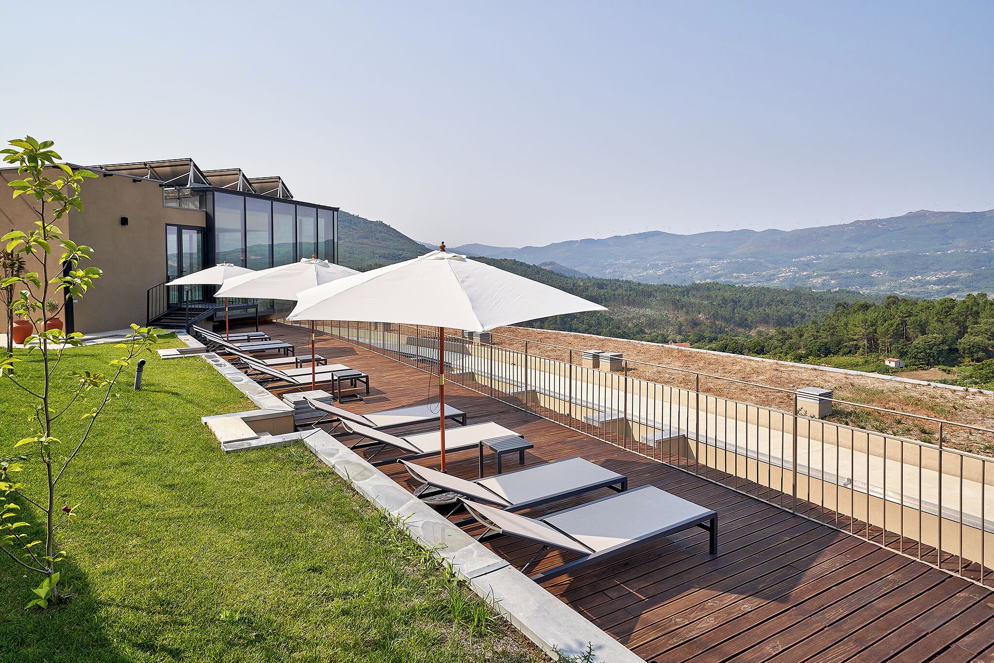 A rooftop terrace with sun loungers and umbrellas, overlooking a mountainous landscape.