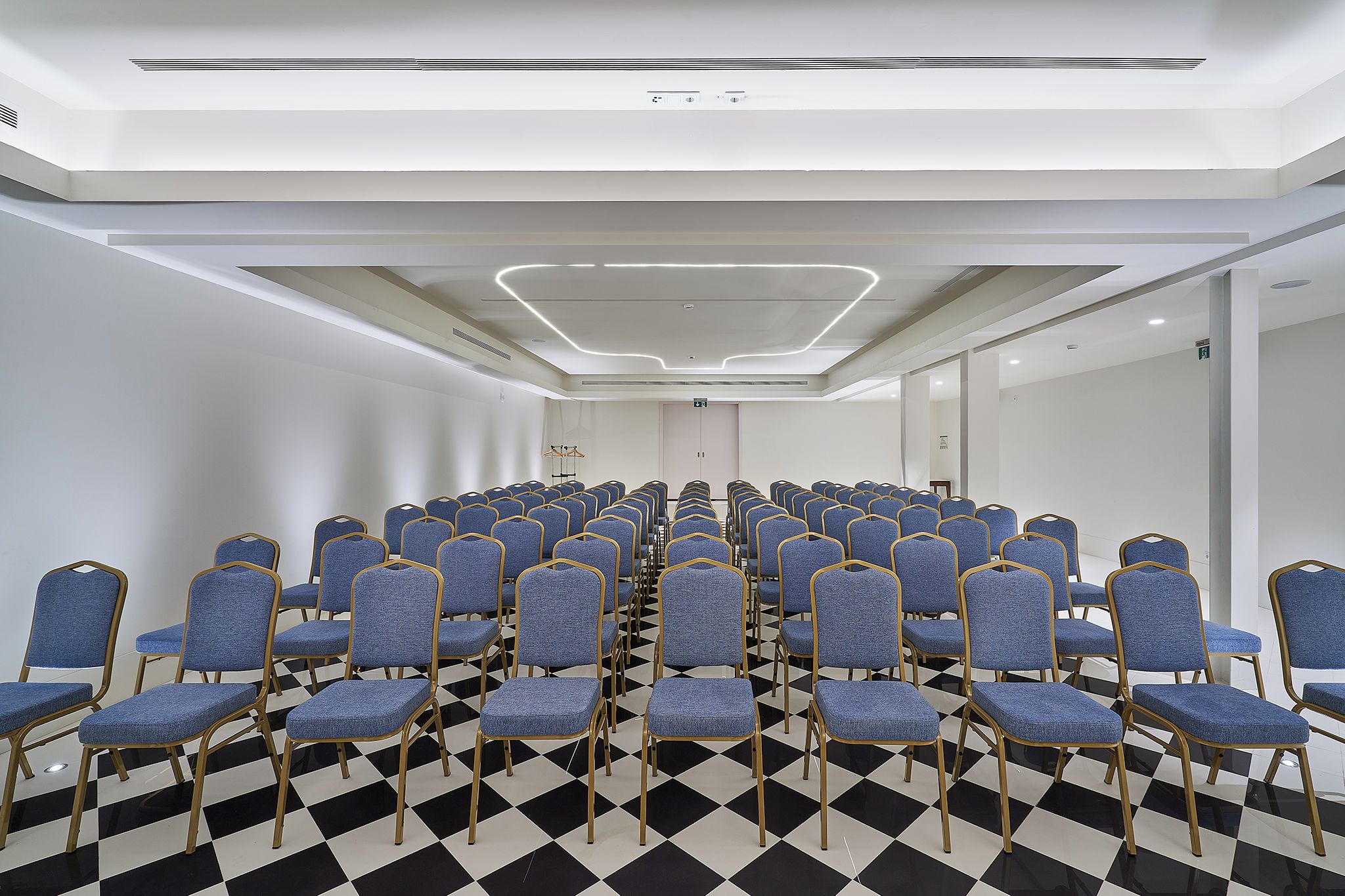 A conference room with rows of blue chairs, a checkered floor, and a modern ceiling design.