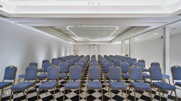 A conference room with rows of blue chairs, a checkered floor, and a modern ceiling design.