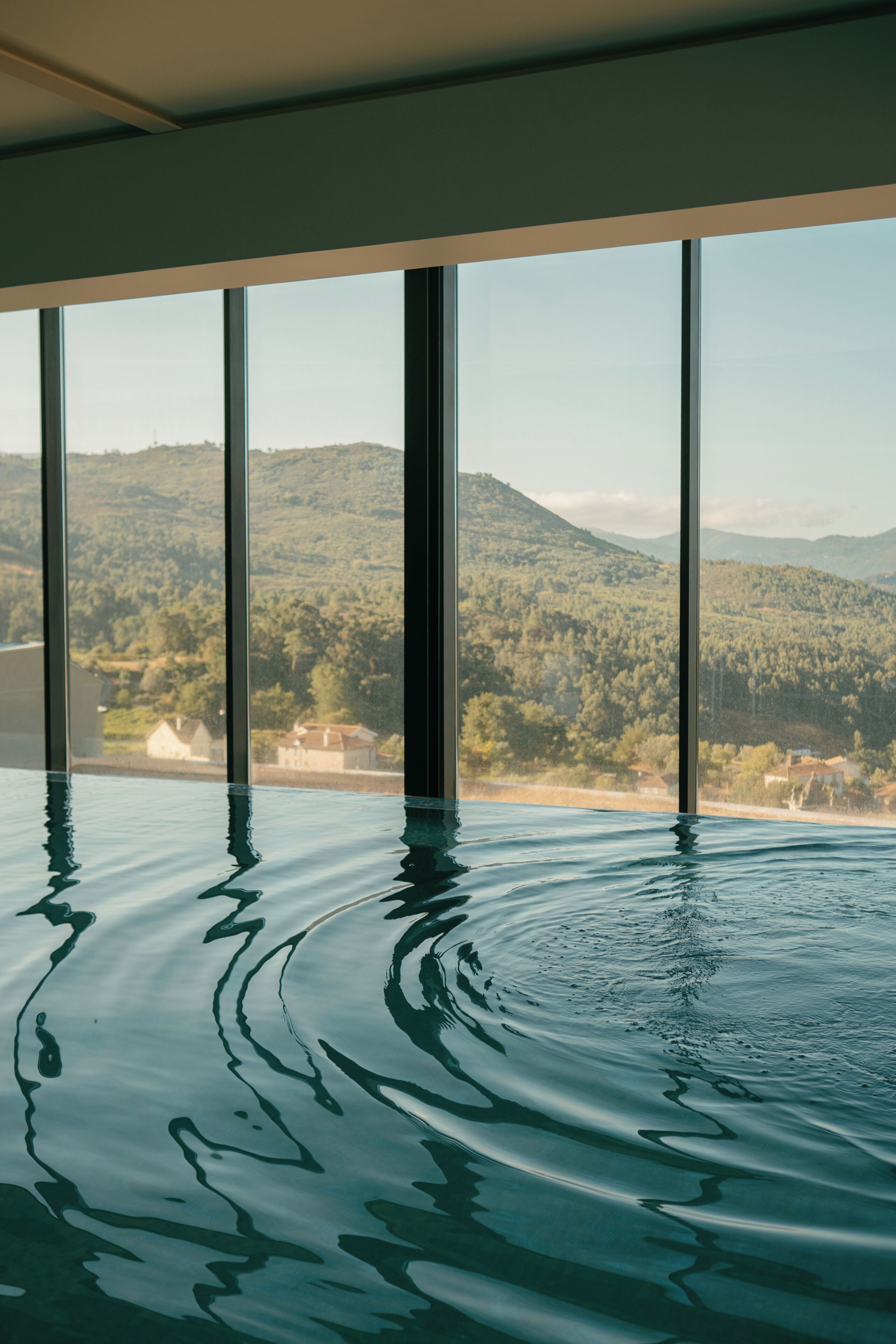 Ein Schwimmbad mit Blick auf eine gebirgige Landschaft durch große Fenster.