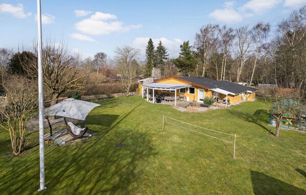 A yellow house with a covered patio, surrounded by a well-maintained lawn and trees.